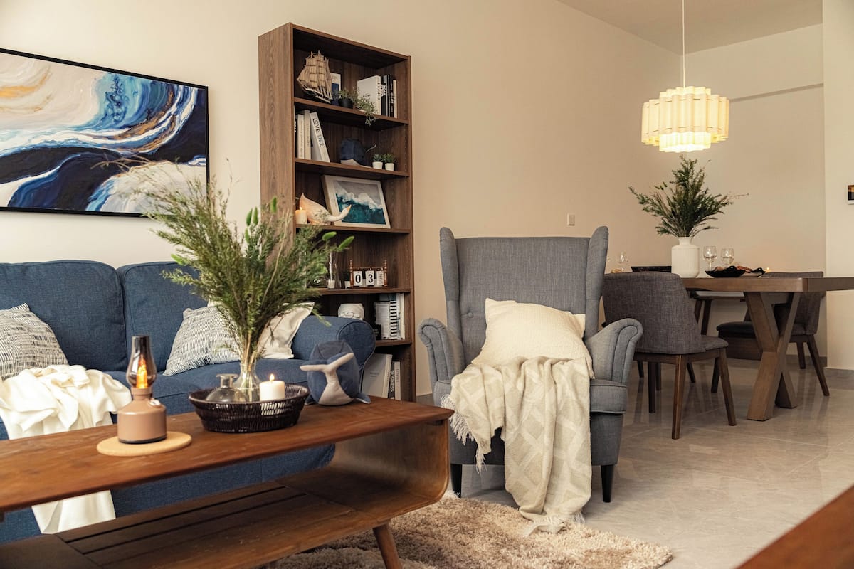 Una sala de estar con sofá, sillón, estantería, mesa de comedor y lámpara colgante.