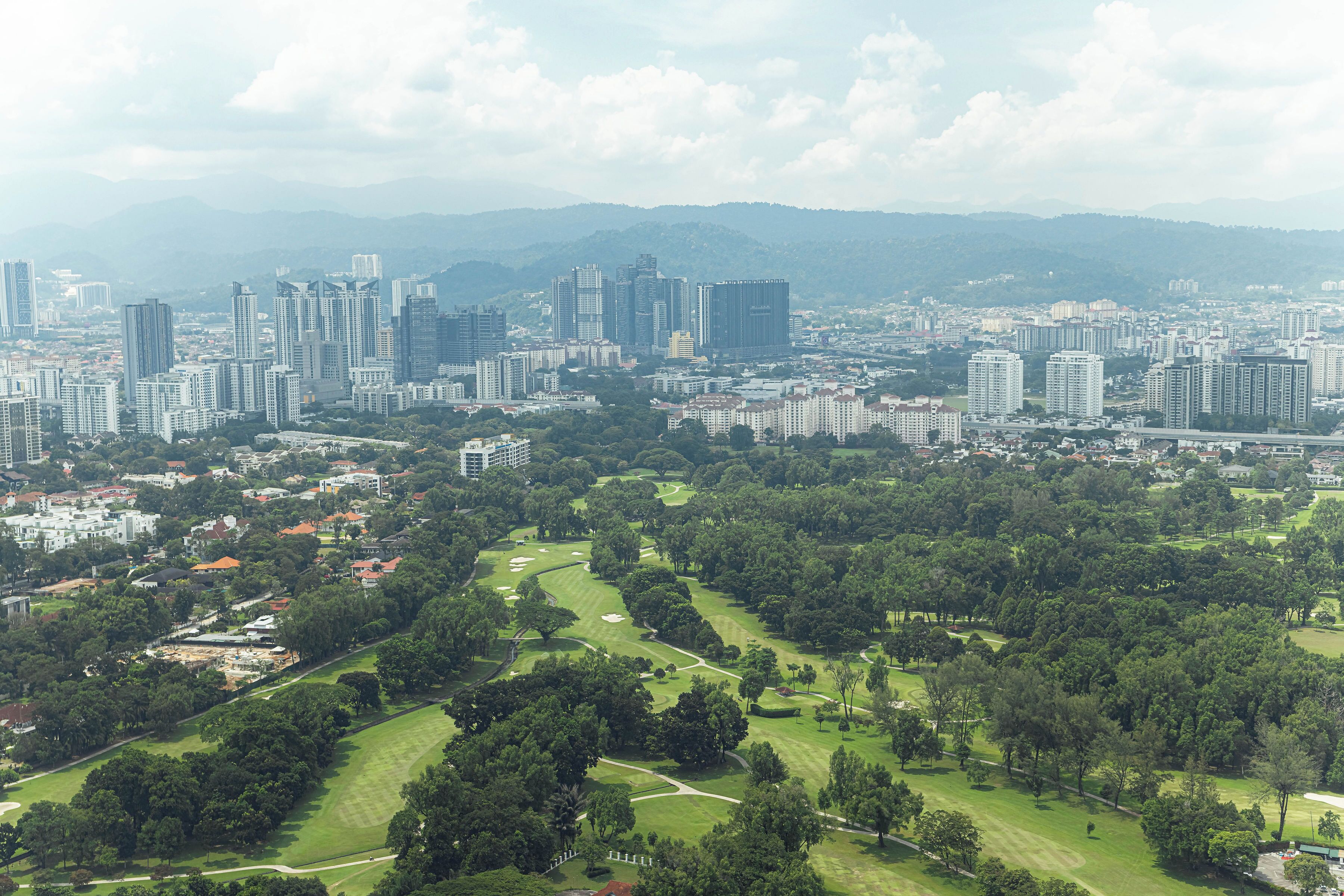 A cityscape with high-rise buildings, a golf course, and surrounding greenery.