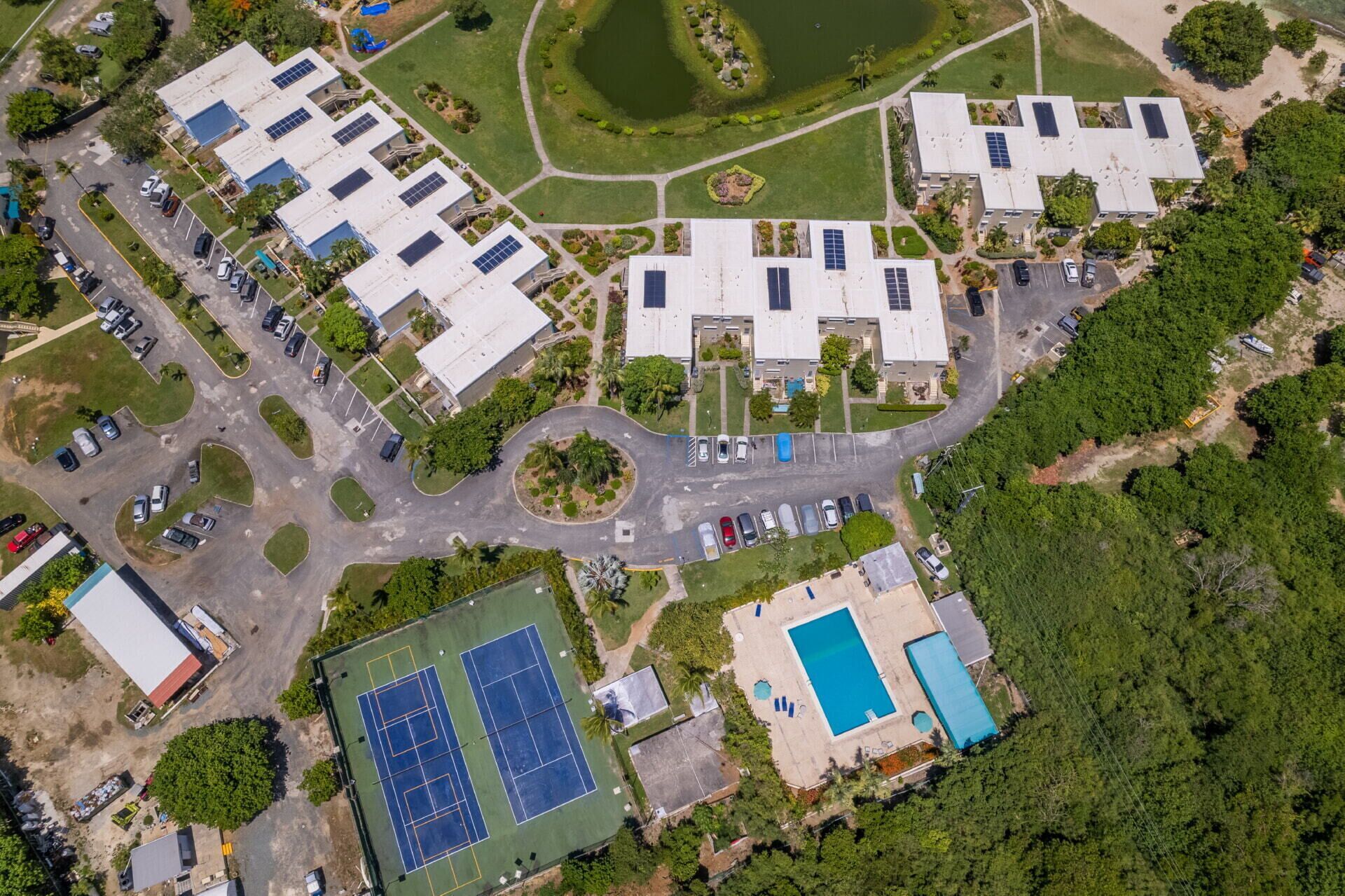 An aerial view of a residential area with multiple buildings, a tennis court, and a swimming pool.