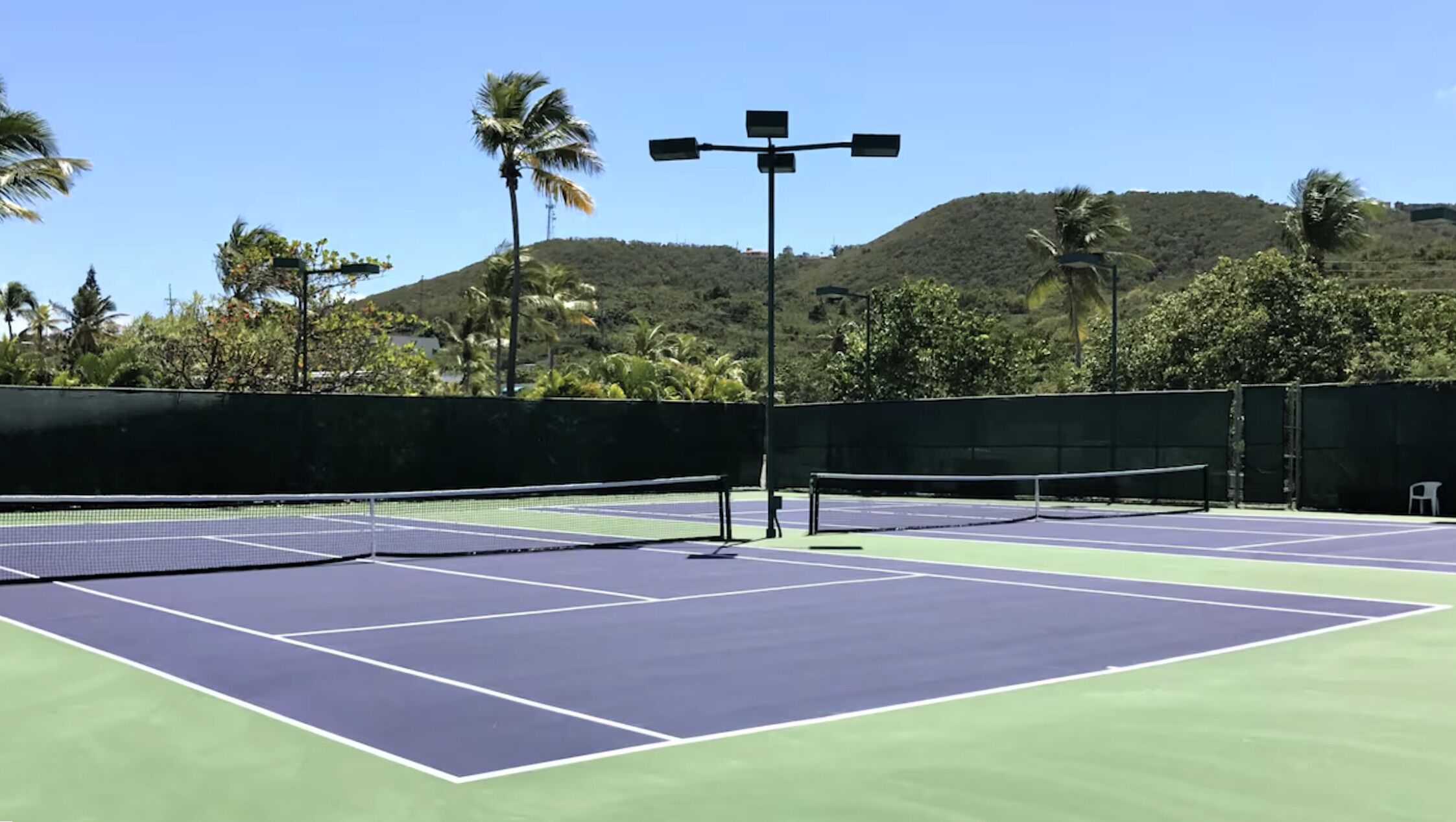 An outdoor tennis court with a net, benches, and a solar-powered light post.