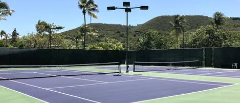 An outdoor tennis court with a net, benches, and a solar-powered light post.