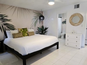 Relax in this serene bedroom with a large bed, dresser, and round mirror, surrounded by lush greenery.