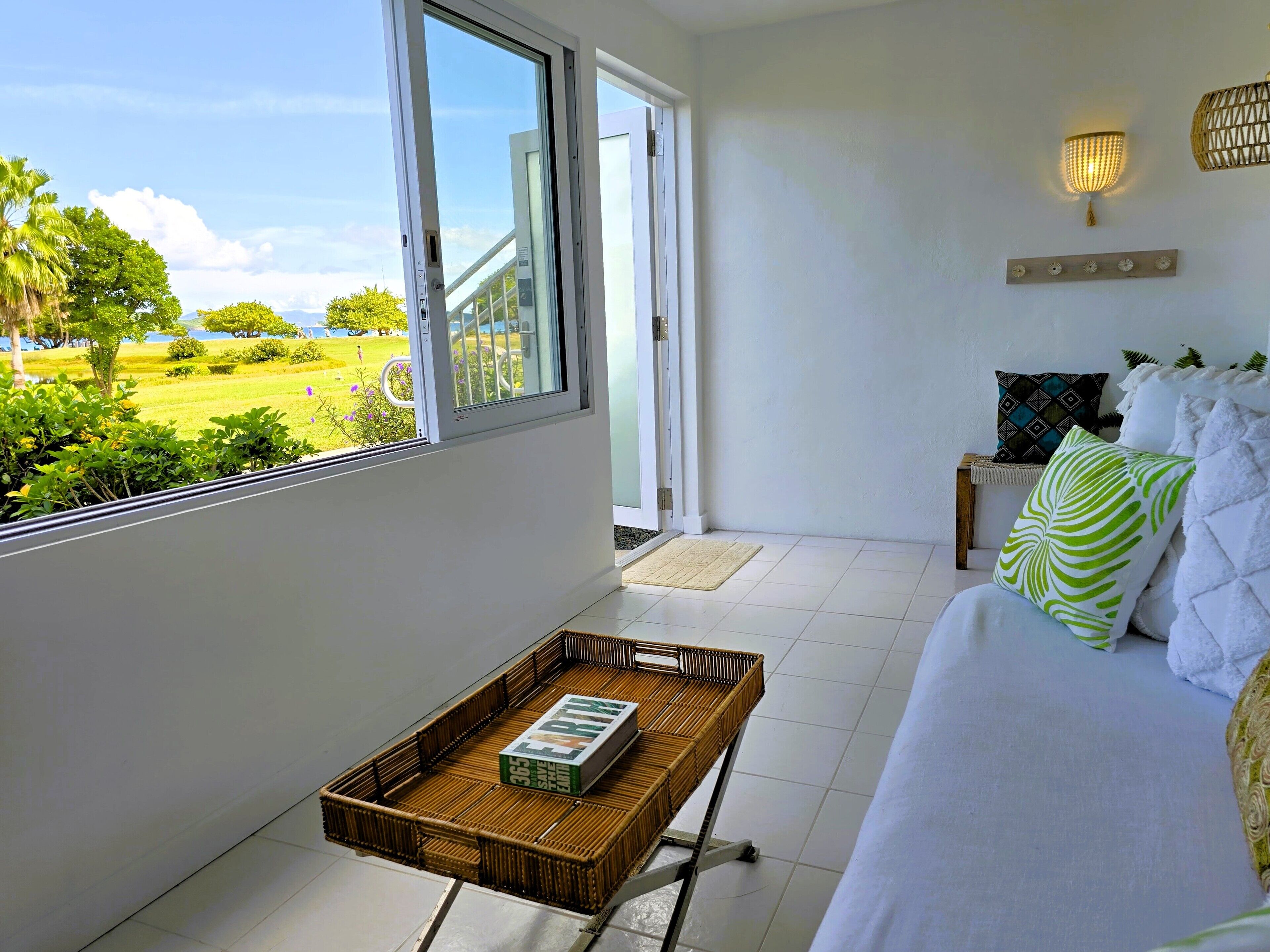 A balcony with a wicker table, a white sofa, and a view of a green landscape.