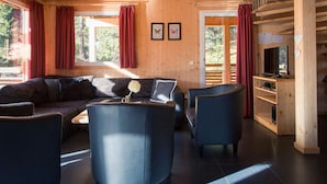 Uma sala de estar aconchegante com um sofá, duas poltronas, uma mesa de centro e uma TV sobre um suporte de madeira.