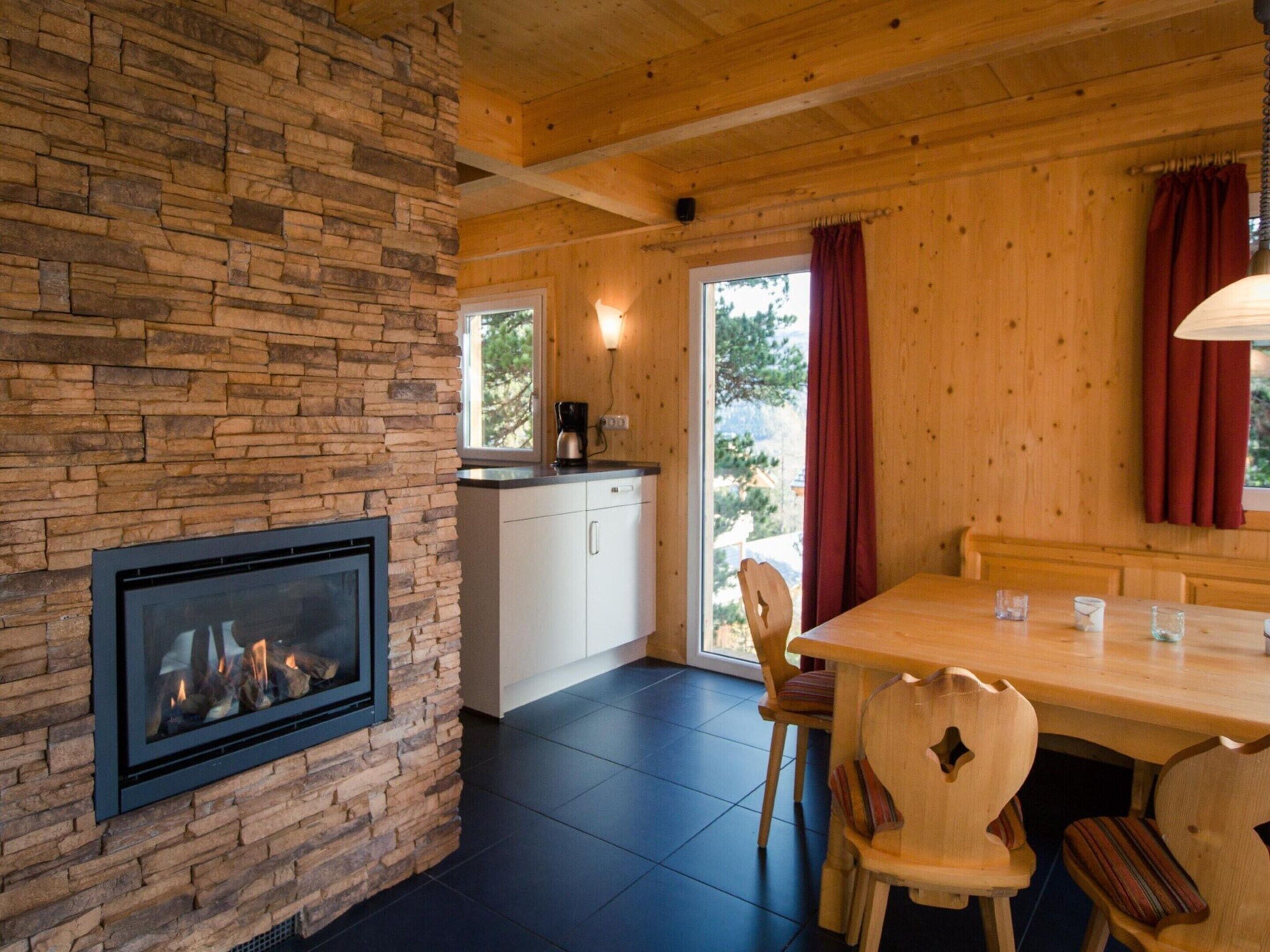 A cozy room with a stone fireplace, wooden ceiling, and a dining area with chairs and a table.