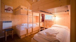 Um quarto de cabana de madeira acolhedor, com beliches, uma escrivaninha e janela com cortinas.