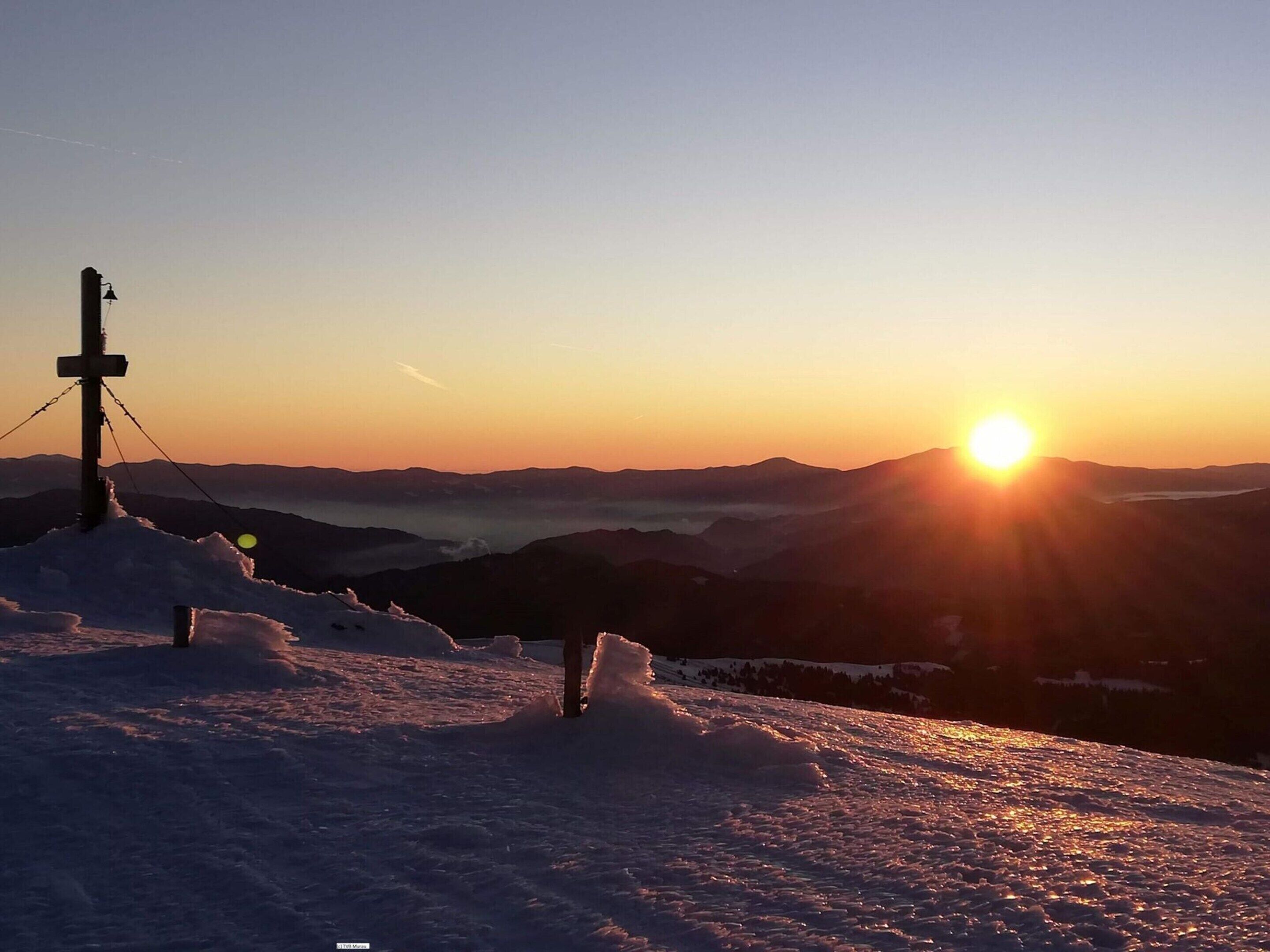 A snowy mountain landscape with a sunset and a cross structure.