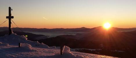 A snowy mountain landscape with a sunset and a cross structure.
