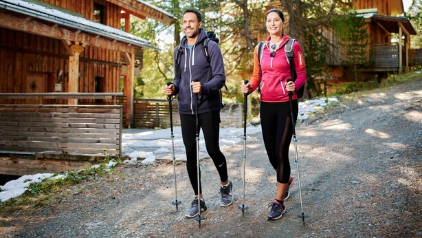 Two people hiking with trekking poles on a gravel path beside wooden cabins. - Apartment in Pine Forest Near Ski Slopes (Stadl-Predlitz)