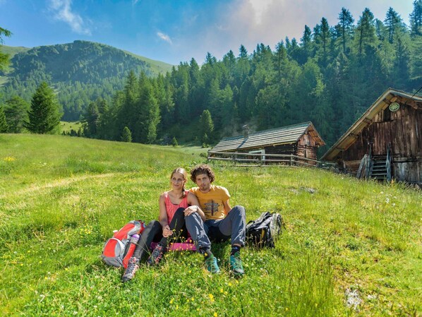 Una pareja sentada en un campo de hierba, con una cabaña de madera al fondo.