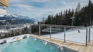 Una vasca idromassaggio con vista su un paesaggio montano innevato e una pista da sci.