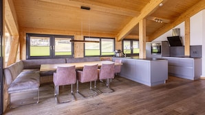 Una cucina moderna con soffitto in legno, una zona pranzo con una panca e sedie, e vista sull'esterno.
