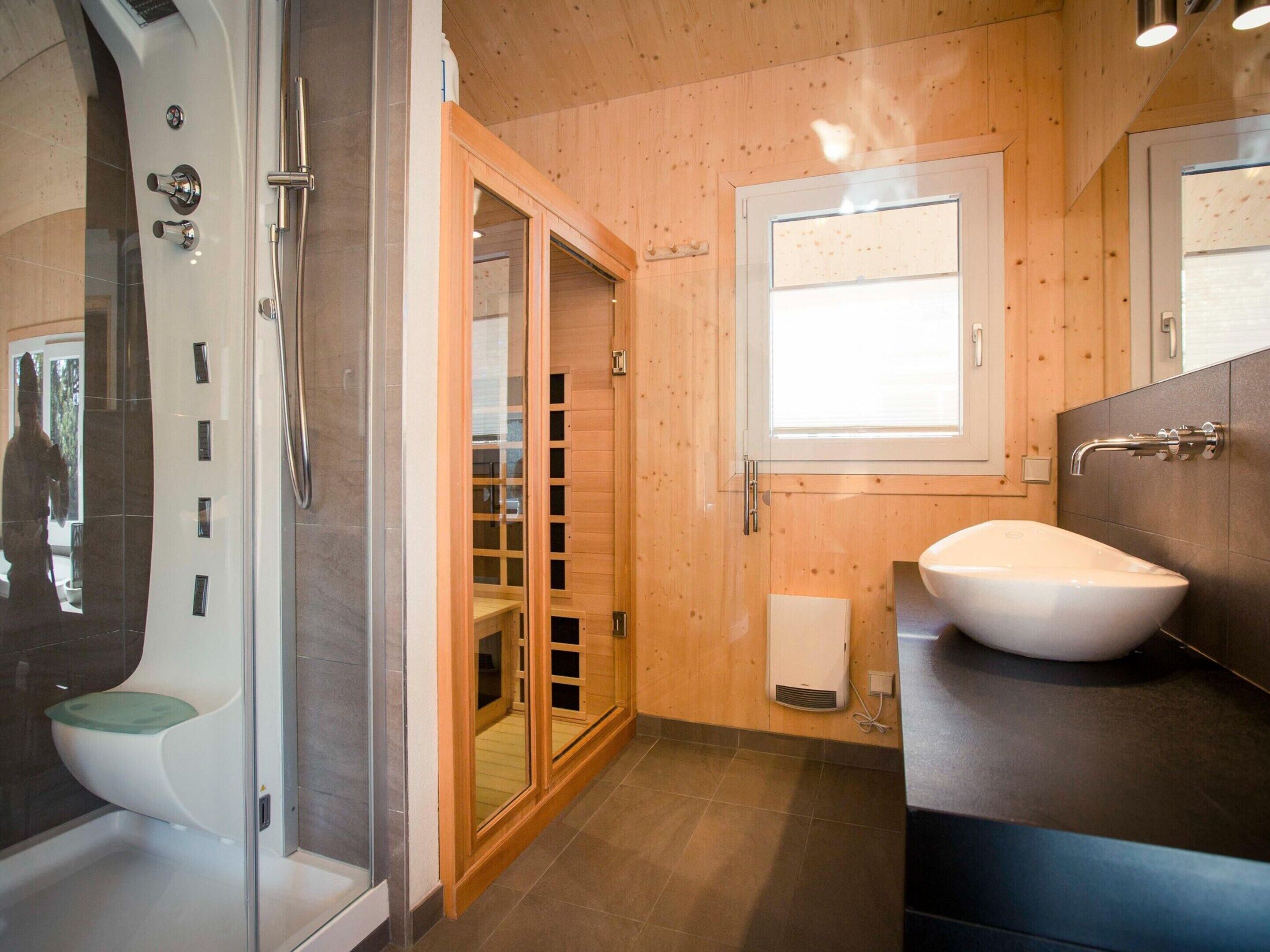 Une salle de bain moderne dotée d’une douche à parois de verre, d’un meuble-lavabo en bois avec un vasque blanche et d’une grande fenêtre laissant entrer la lumière naturelle.