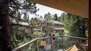 A wooden deck with a hammock chair, overlooking a forested area with multiple cabins. - Cosy Chalet With Infrared Sauna (Stadl-Predlitz)