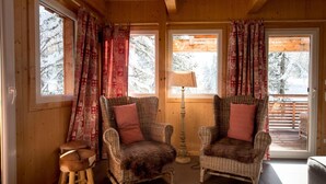 A cozy cabin interior with two wicker armchairs, a small stool, and a lamp.