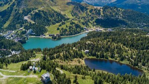 A mountainous landscape with a lake, surrounded by dense forests and a few buildings.