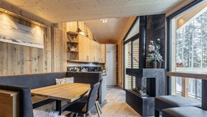 A modern kitchen with wooden cabinets, a dining area with a wooden table and chairs, and a large window offering a view of the outdoors.