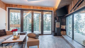 A modern living room with a large sliding glass door leading to a deck, a fireplace, and a television mounted on the wall.