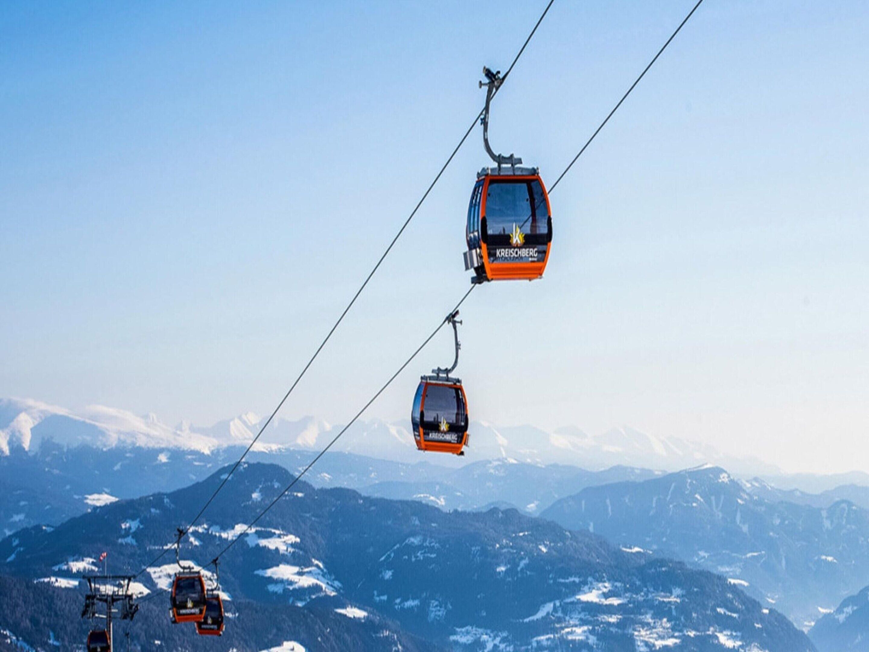 Un sistema de teleférico con varias cabinas suspendidas por cables, con montañas al fondo.