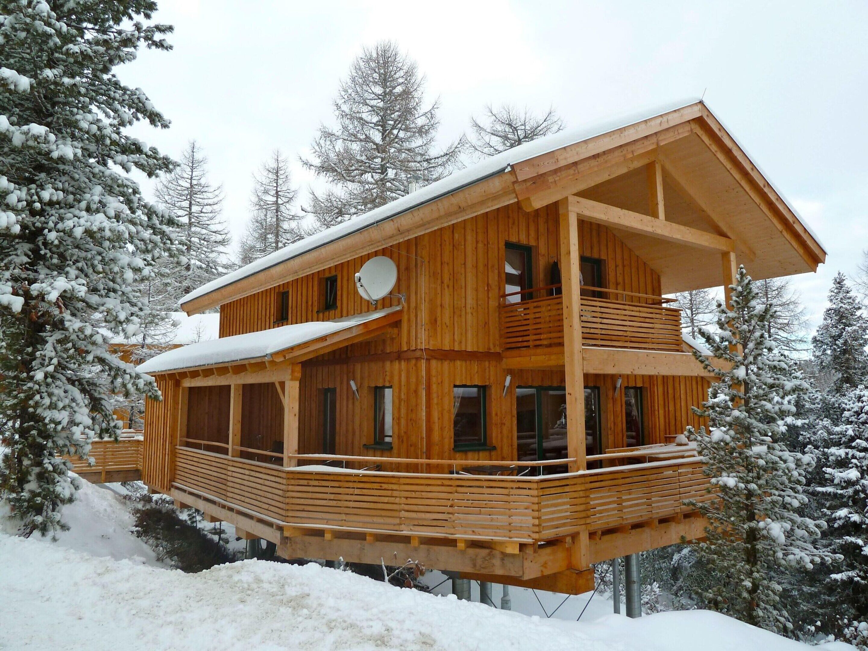 A two-story wooden cabin with a balcony, surrounded by snow-covered trees.