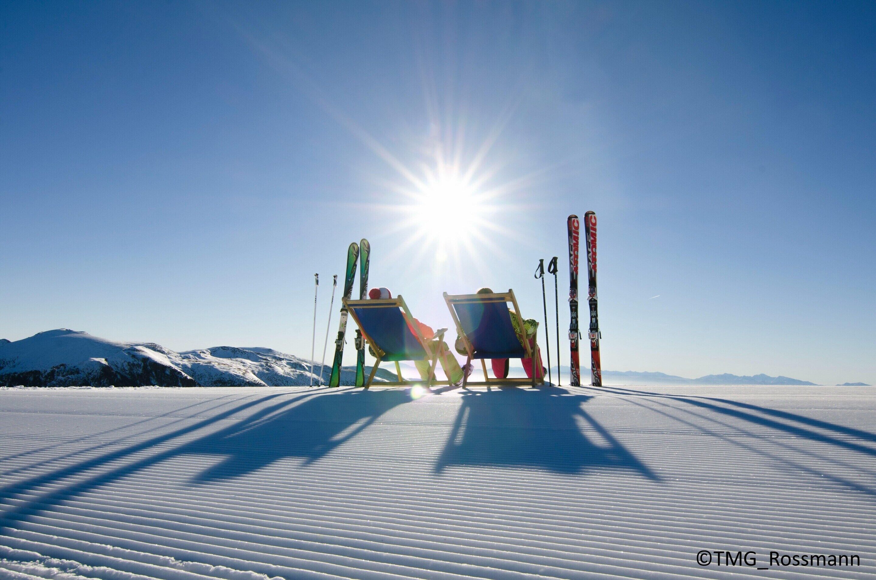 A snowy landscape with two sunlit ski chairs and skis.