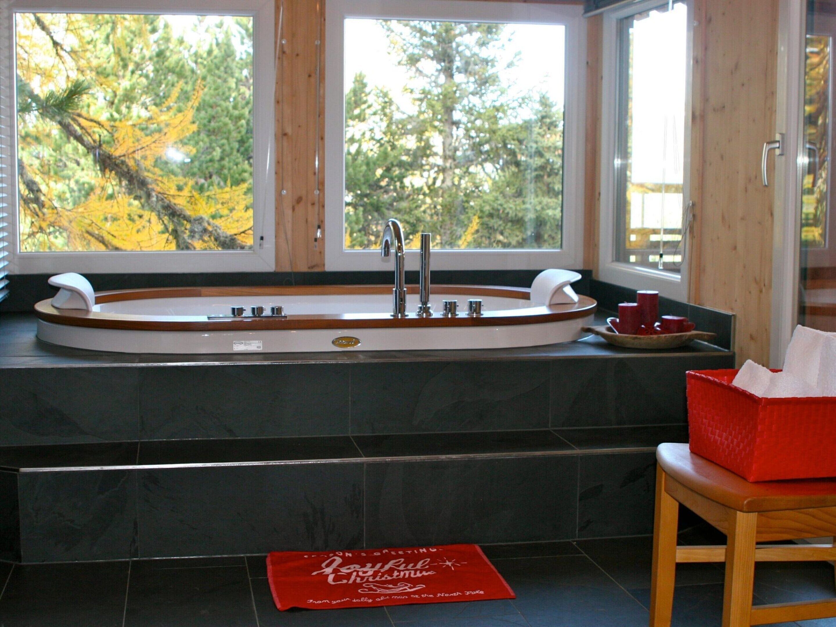 A bathroom with a freestanding bathtub, a window with a view of trees, and a red mat on the floor.