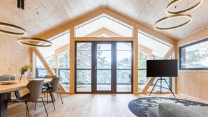 A spacious room with a wooden ceiling, large windows, a dining area, and a flat-screen TV. - Modern Chalet With Indoor Sauna (Stadl-Predlitz)
