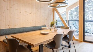 A modern dining area with a wooden table, four chairs, and a large window offering a view of the outdoors. - Modern Chalet With Indoor Sauna (Stadl-Predlitz)