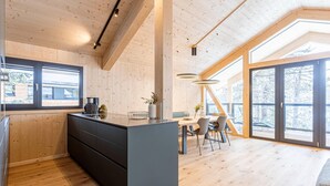 A modern kitchen with wooden walls, a central island, and a dining area with a large window. - Modern Chalet With Indoor Sauna (Stadl-Predlitz)