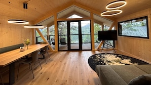 A spacious room with a wooden ceiling, a large window, a wooden desk, a sofa, and a TV on a tripod. - Modern Chalet With Indoor Sauna (Stadl-Predlitz)