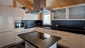 A modern kitchen with a central island, built-in oven, and a window overlooking a snowy landscape. - Lovely Chalet With Sauna (Stadl-Predlitz)