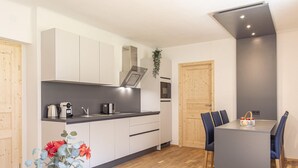 Eine moderne Küche mit weißen Schränken, einer grauen Arbeitsplatte und einem eingebauten Backofen. Es gibt einen Essbereich mit Tisch und Stühlen sowie eine Vase mit Blumen auf dem Tisch.