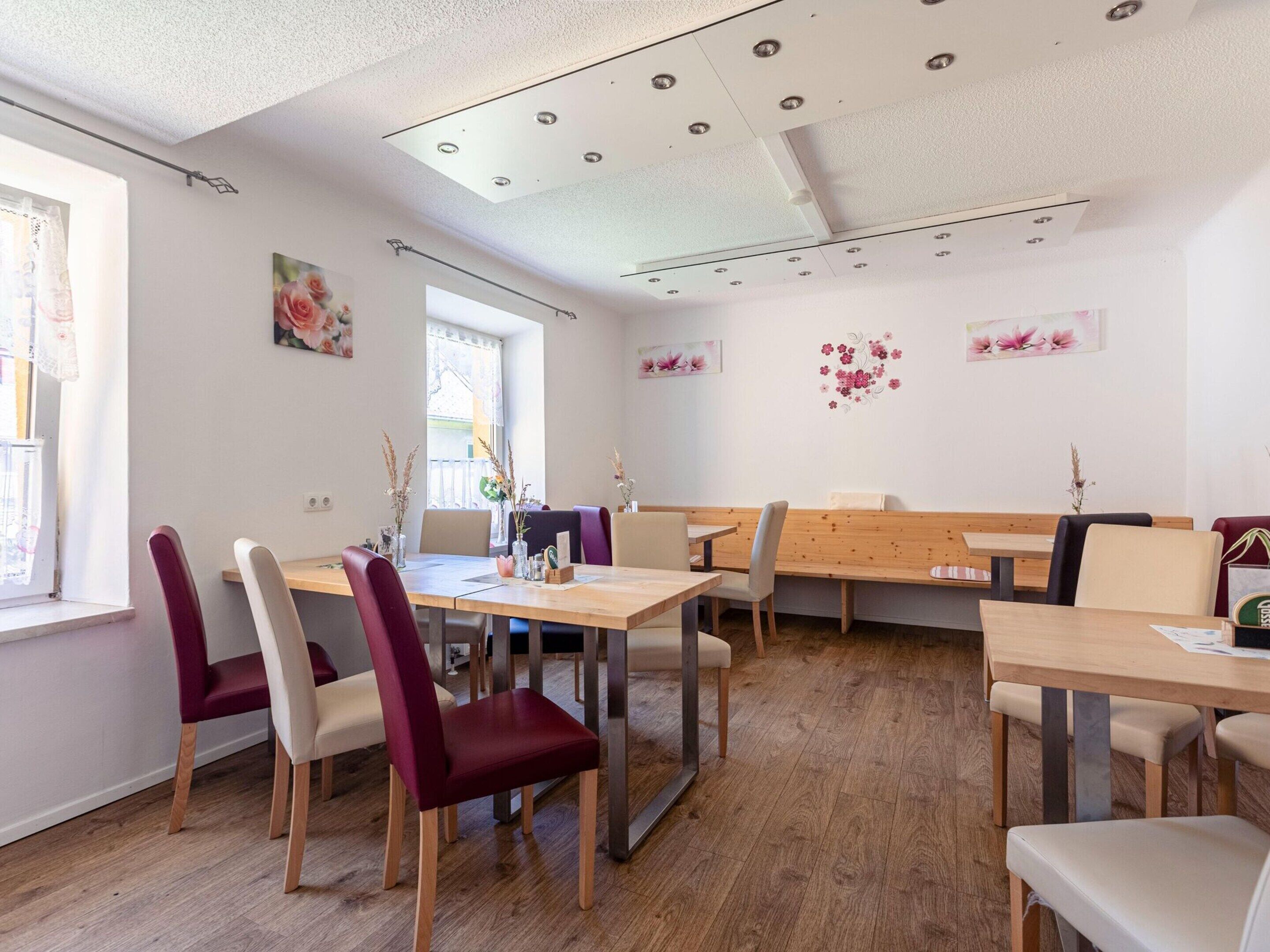 A dining area with wooden tables and chairs, a ceiling with recessed lighting, and floral wall art.