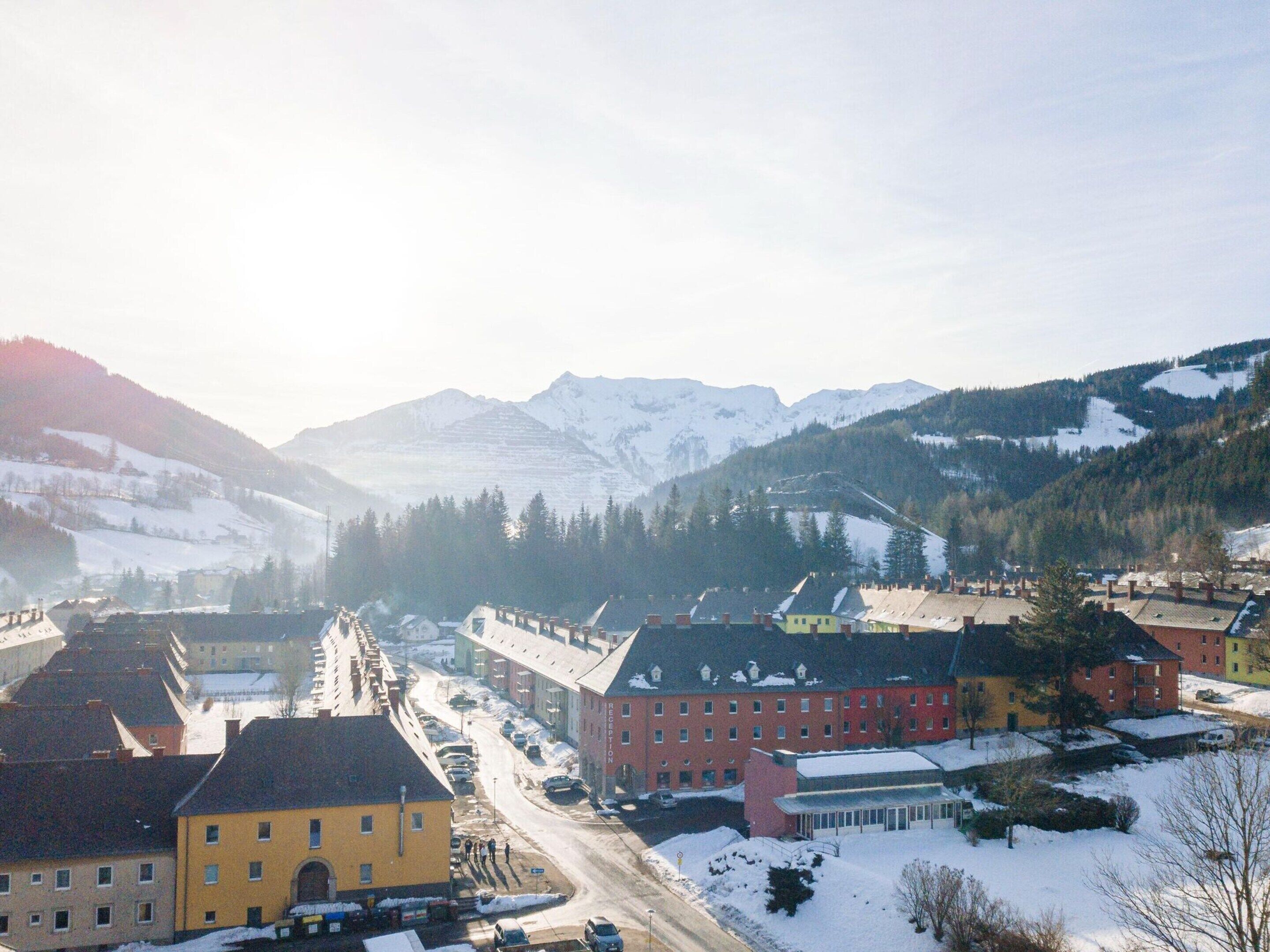A town with buildings, a road, and snow-covered mountains in the background.