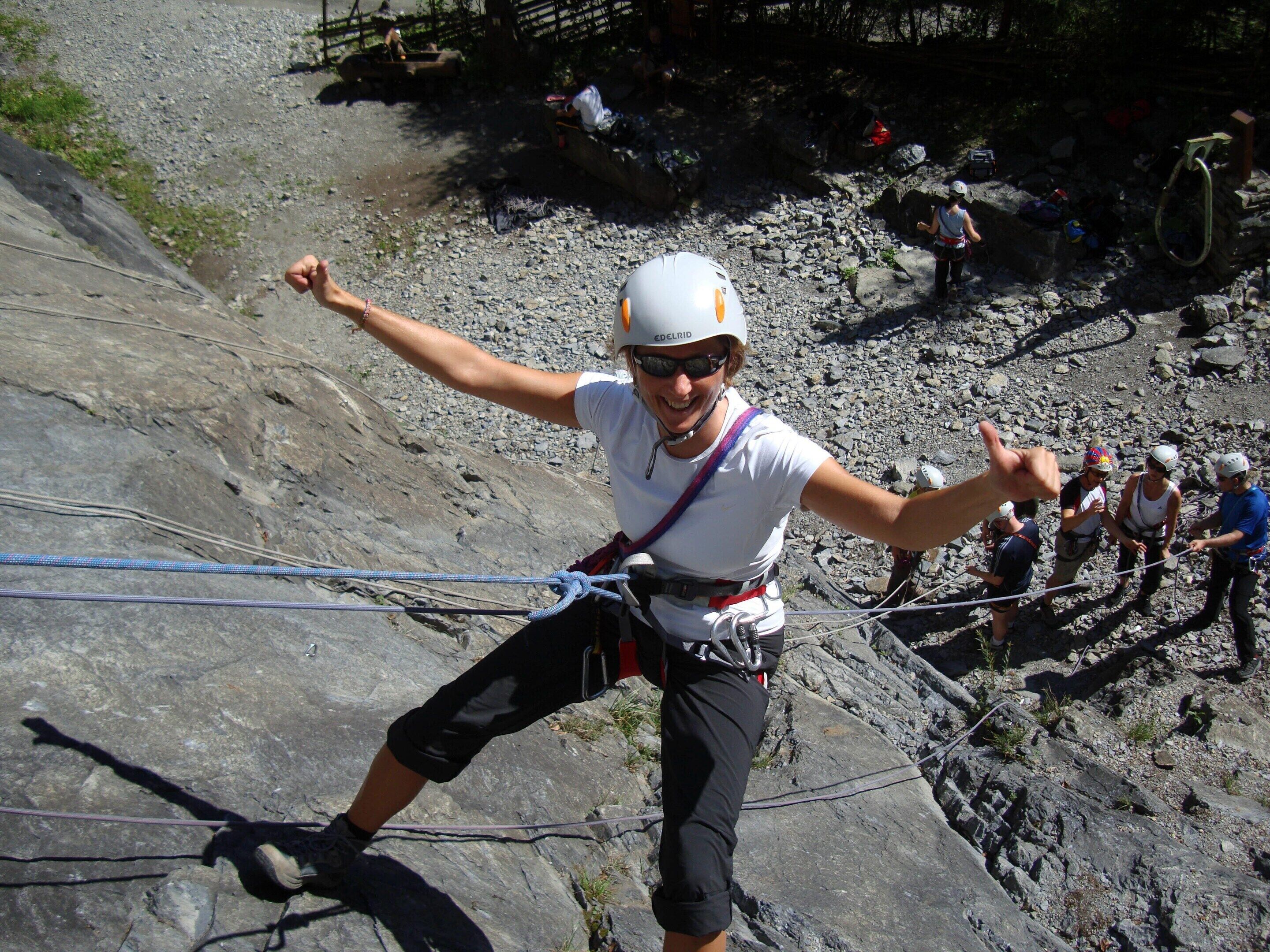 Une personne qui descend une pente rocheuse en rappel, équipée d’un harnais et d’un casque.