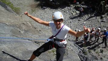 Une personne qui descend une pente rocheuse en rappel, équipée d’un harnais et d’un casque.