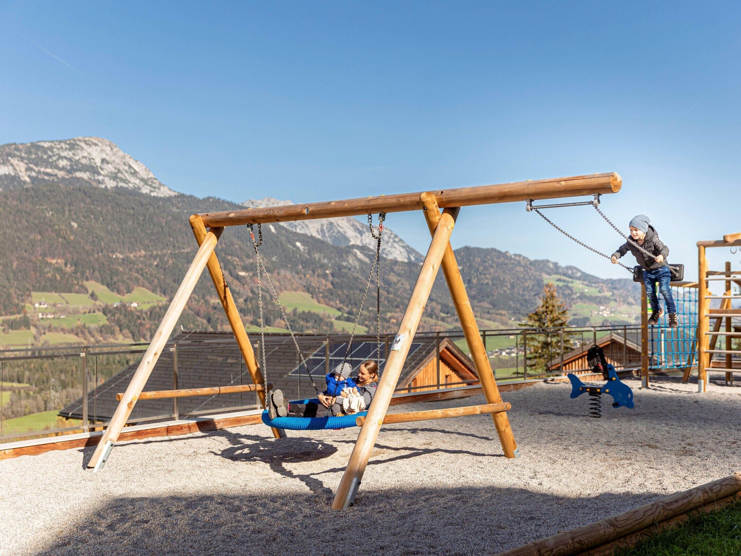 A playground with swings and climbing structures, set against a mountainous backdrop.