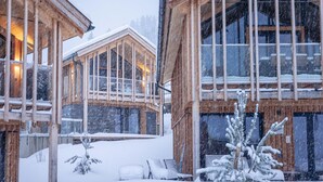 Une cabane en bois dotée de grandes fenêtres et dont l’extérieur est recouvert de neige.