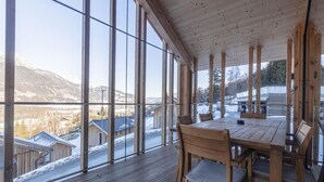 Une terrasse en bois avec une table et des chaises, donnant sur un paysage enneigé et des montagnes.