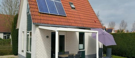 Een huis met een hellend rood dak, witte bakstenen muren en een overdekte patio met een tafel en stoelen.