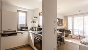 A modern kitchen with a microwave, stove, and dishwasher. There is a dining area with a table and chairs, and a living room with a sofa and a lamp. - Apartment Near Ski Slope (Schladming)