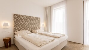 A double bed with a patterned headboard, bedside lamps, and a view of a window with sheer curtains. - Apartment Near Ski Slope (Schladming)