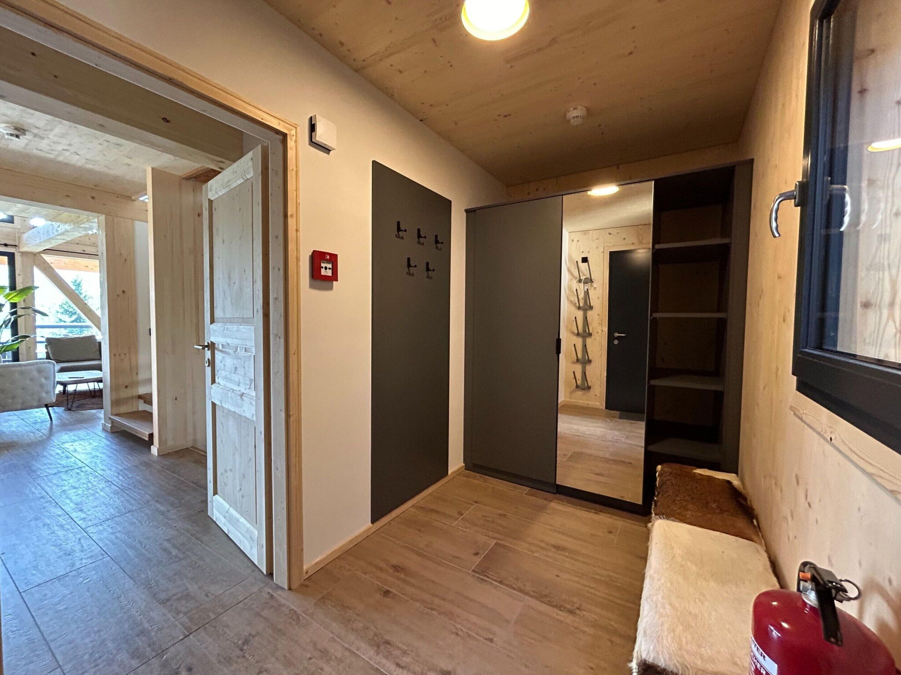 Un couloir doté d’un plancher en bois, d’un banc, d’un extincteur et d’une porte équipée d’un système d’alarme incendie.