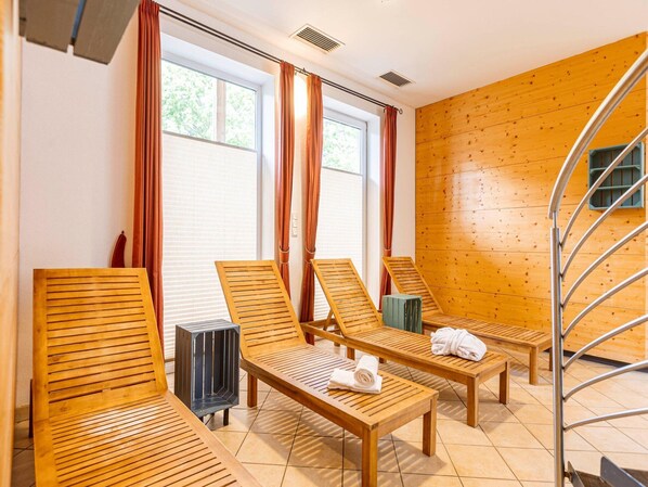 A room with wooden flooring, three wooden lounge chairs, a small table, and a spiral staircase.