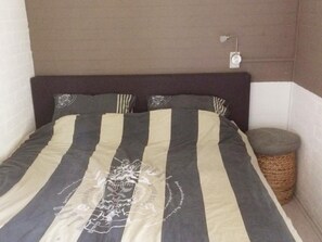 Un lit avec une literie à rayures et un motif décoratif au centre, une lampe de chevet et un panier en osier.