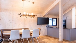A modern interior with a wooden ceiling, a dining area with a table and chairs, a kitchen with a flat-screen TV, and a large window. - Inviting Chalet With Indoor Sauna (Stadl-Predlitz)