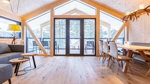 A spacious room with a high ceiling, wooden flooring, a dining area with a table and chairs, and large windows offering a view of the outdoors. - Inviting Chalet With Indoor Sauna (Stadl-Predlitz)