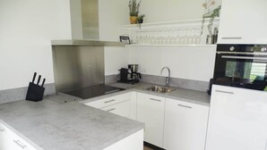A modern kitchen with white cabinets, a stainless steel range hood, a coffee maker, and a dishwasher. - Holiday Home With Pet-friendly Garden (Breskens)