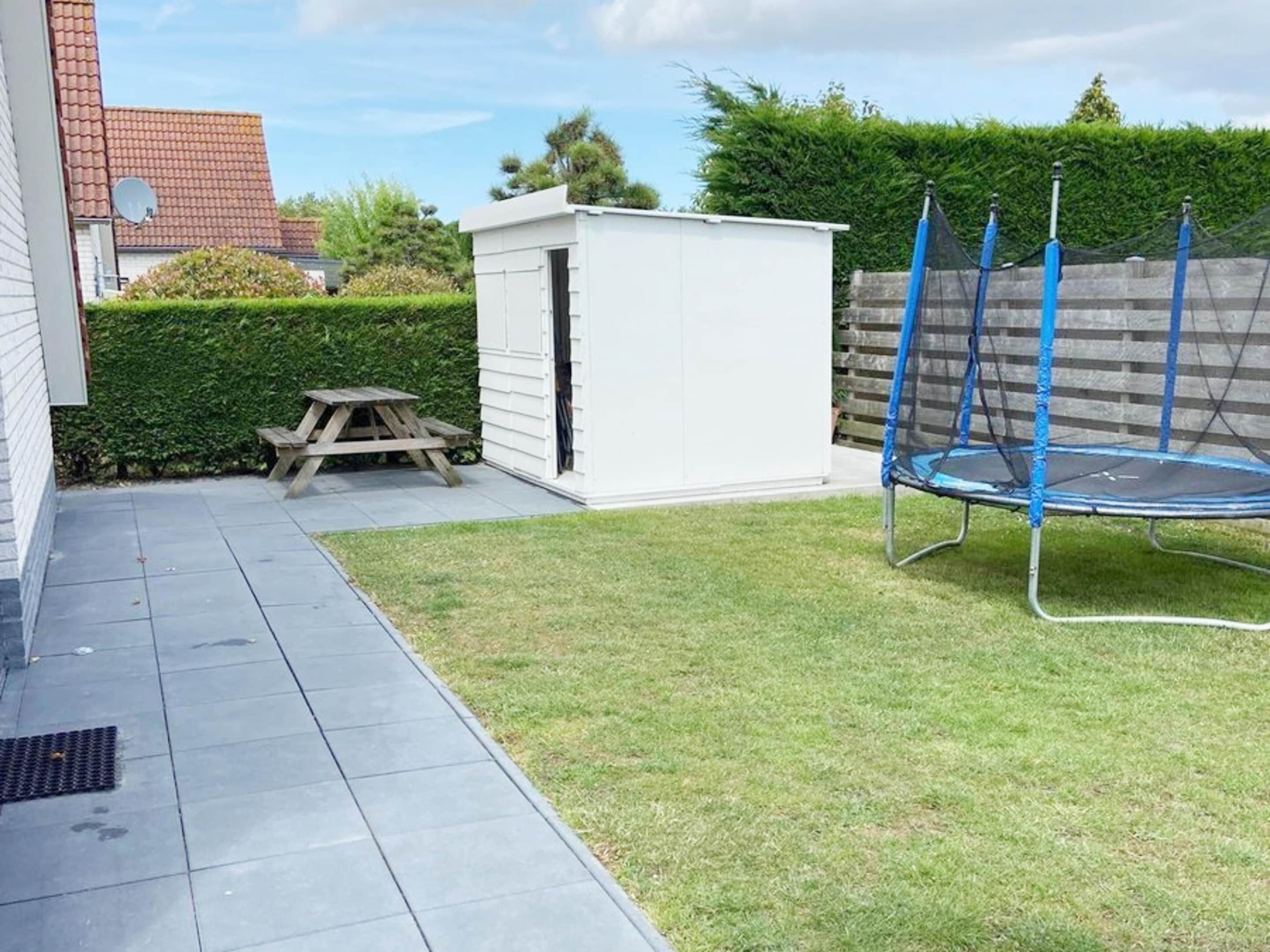 Un patio trasero con un trampolín, un cobertizo pequeño, una mesa de picnic y un sendero pavimentado.