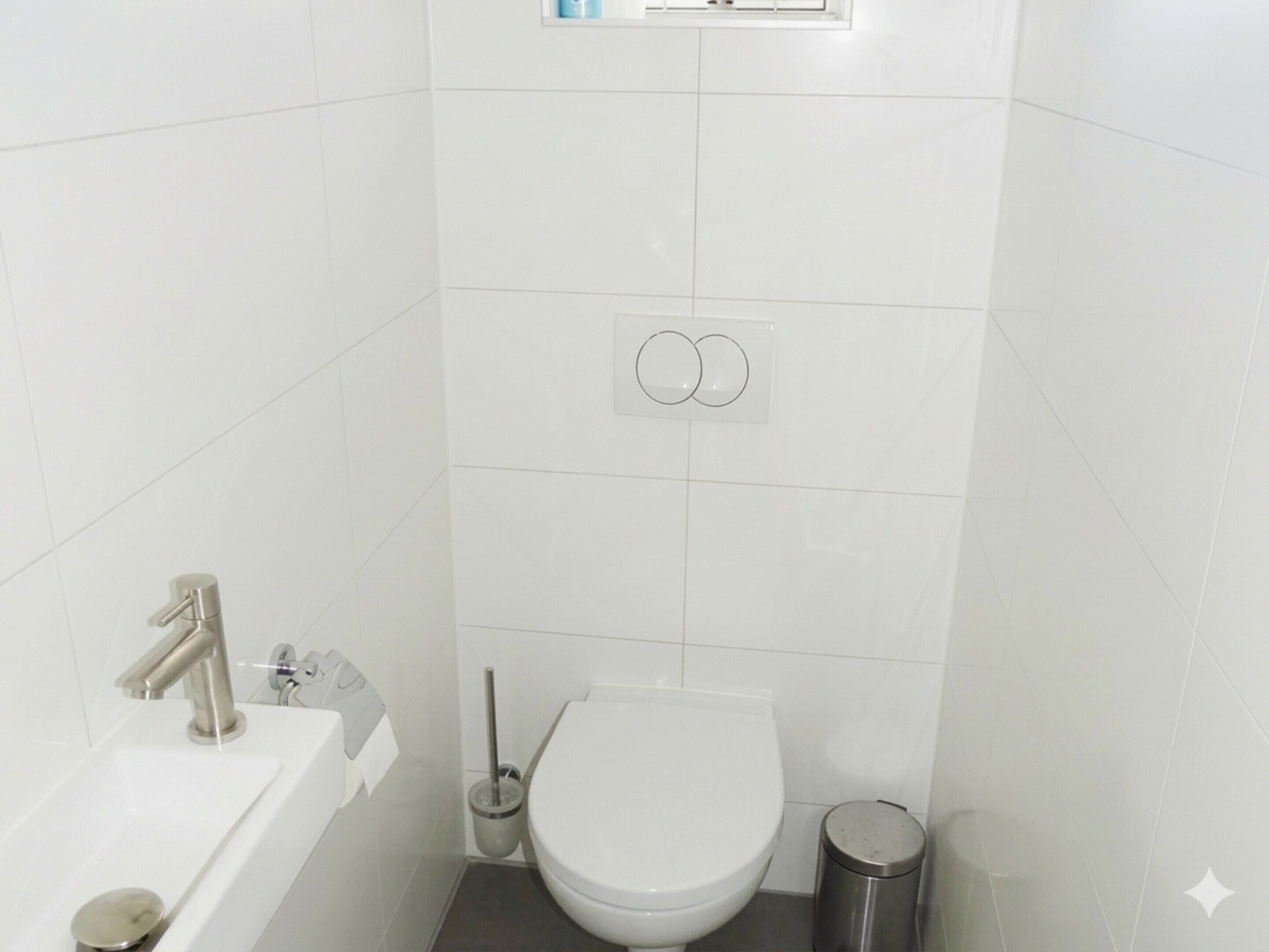 Casa de banho com lavatório branco, sanita e um contentor de lixo.